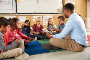 Diverse students sitting on floor with teacher reading a book together