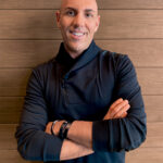 Photo of Erik Lepis with arms crossed leaning against a wall portrait shot.